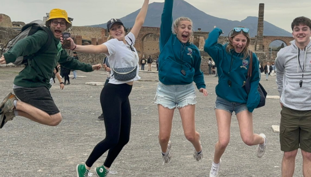 Picture of school students and a teacher jumping in the air with Mount Vesuvius in the background