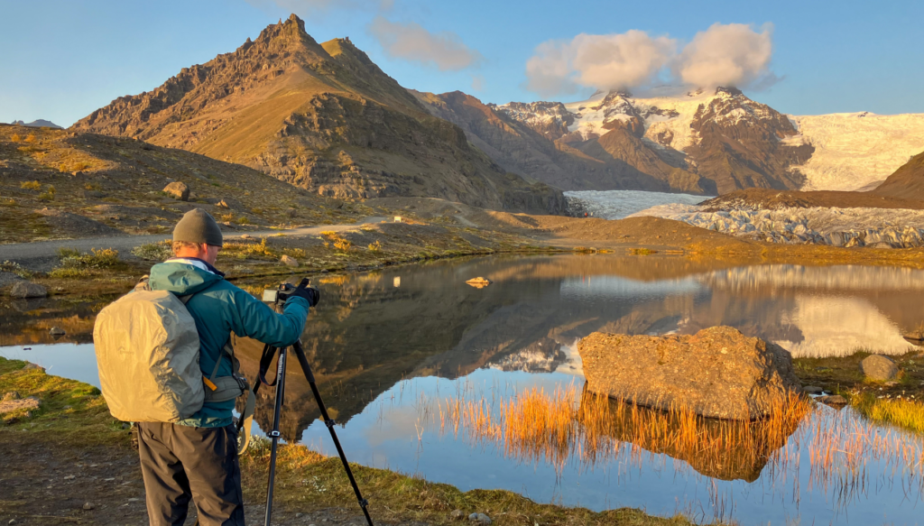 Picture of someone taking a picture of icelandic glacier using a tripod at sunset