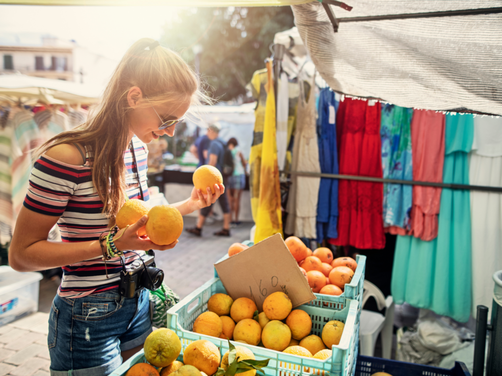 Picture of a girl holding oranges and looking at a stall in a spanish market