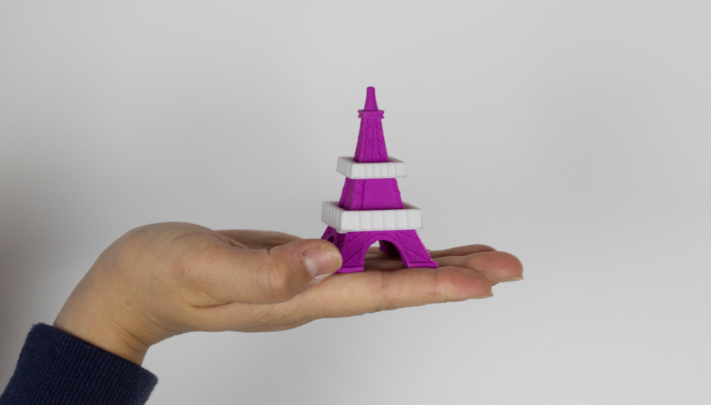 Picture of a hand holding a purple plastic Eiffel Tower model