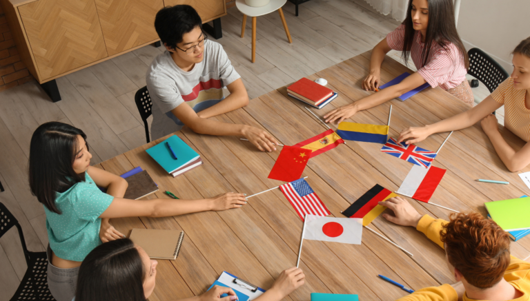 Picture of students sat around a desk, in the centre of the desk there is a variety of flags from different countries